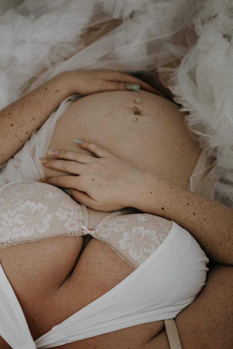 Maternity Boudoir Photography a pregnant woman in a white bra laying on a bed